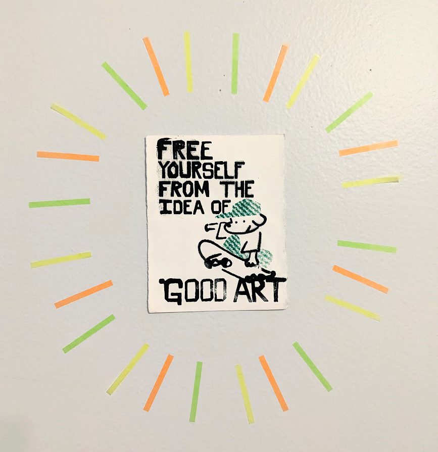 A photo of a frameless picture adhered to the wall. It's a picture of a dog where a t-shirt, green cap, and green pants, doing a kickflip on a skateboard. The text on this image says 'FREE YOURSELF FROM THE IDEA OF GOOD ART.' There are little green, orange, and yellow lines radiating from the picture (they are sticky post-it markers that I stuck all around the picture).